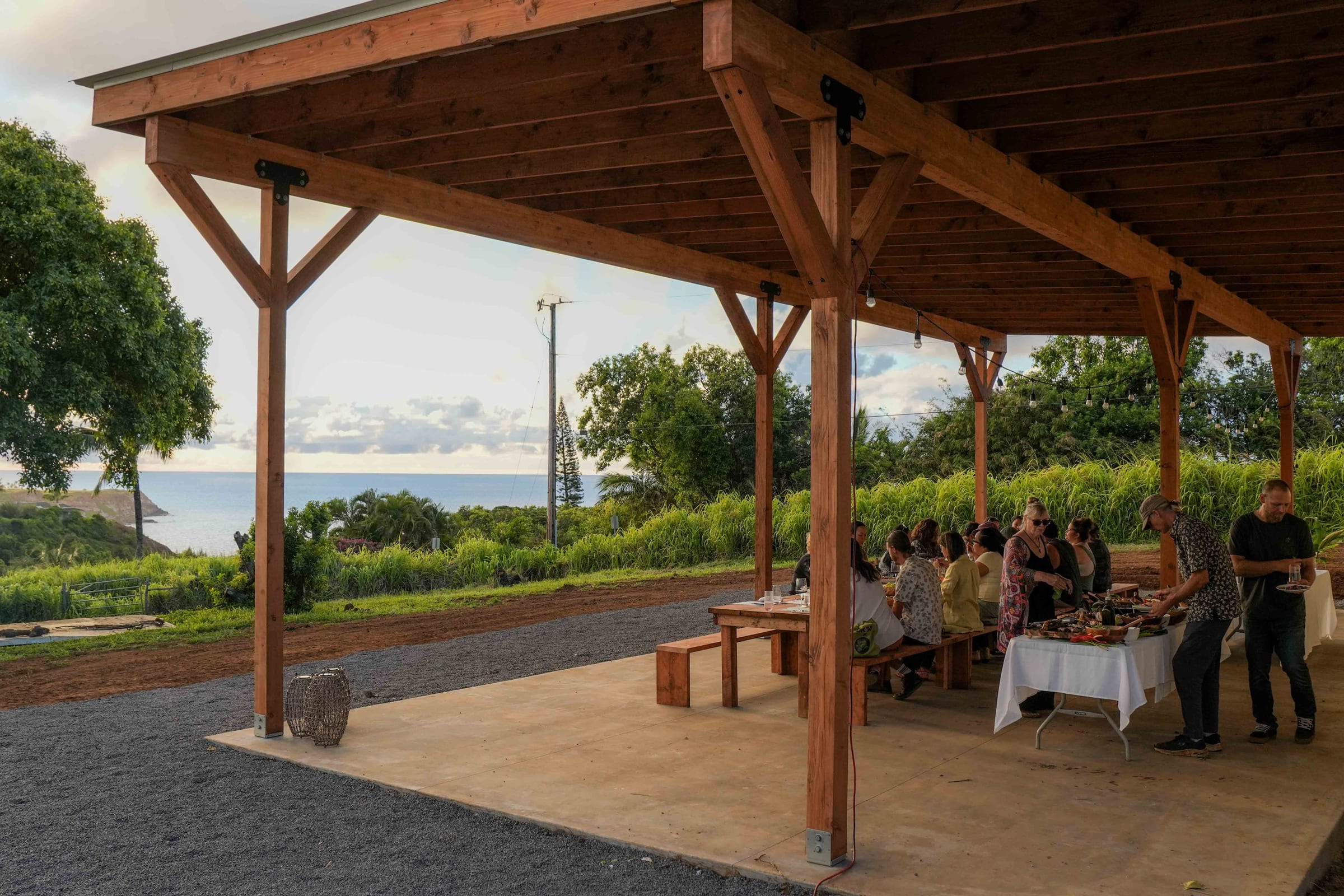 The open-air pavilion framing the ocean and the north-shore cliff, guests at the long table to the right